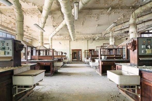 abandoned laboratory with wooden fume cupboards, long pipes run along the ceiling to exhaust the fumes