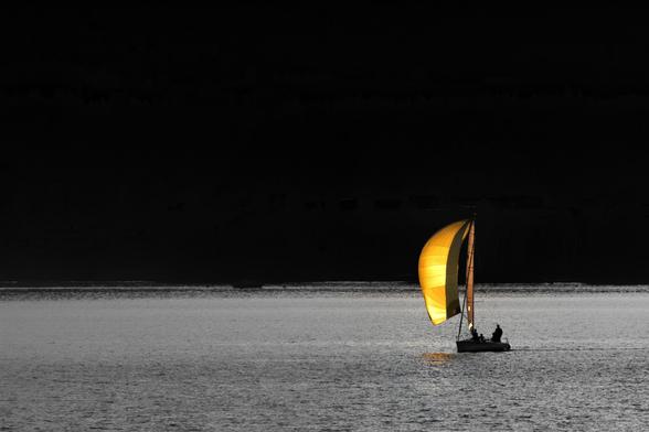 Schwarzweissfotografie mit Selektivfarbe Gelb eines Segelbootes unter Spinnaker im Abendlicht.