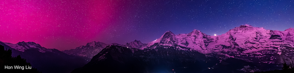 Night panorama of Eiger, Mönch and Jungfrau in a pinky northern lights glow.