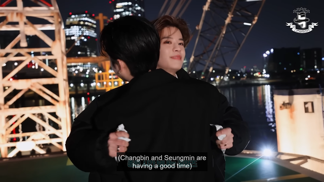 Changbin's hugging Seungmin. They're on the barge on the Han River at night, where they filmed S-Class MV. Seungmin's face is visible over Changbin's shoulder, and he seems to be glowing with happiness.
