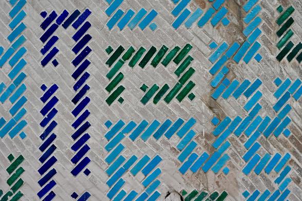 Detail view of a wall decorated with patterns of glazed tiles in different shades of blue and green