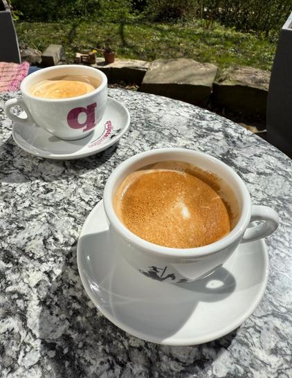 Zwei gefüllte Cappuccinotassen von QuijoteKaffee auf einem Bistrotisch.