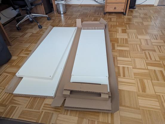A bunch of unassembled white wooden shelf pieces on the floor