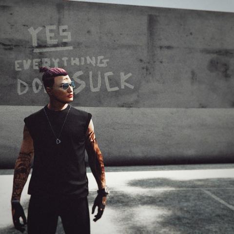 Grand theft auto 5 online Video game screenshot, showing wannabekingpin's main character, a guy in black joggers with a black t-shirt with rolled up sleeves, and a pink undercut sit a little ponytail on top. Aviator glasses, Ds shaped necklace, black leather driver gloves, and many tattoos all over hands, neck, face. In the background there's a walk with graffiti on it that says "yes, everything does suck", word "yes" underscored.