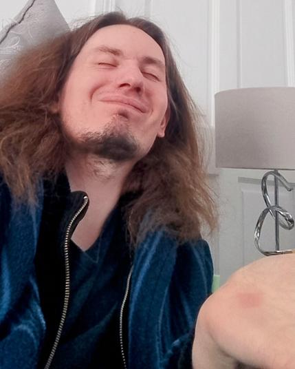 A selfie of me smiling and with my eyes closed along with my hand raised upwards.