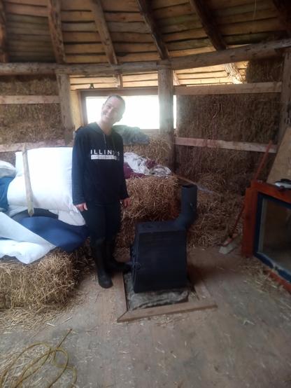 Lucy, for whom we're building the roundhouse, stands by the stove. The walls are still of bare straw, and unused bales still litter the space.