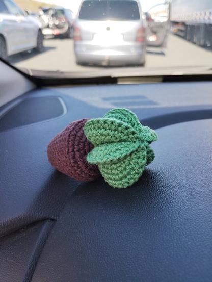 A small crochet cactus sitting on a cars' dash, with a long queue of cars visible through the front window.