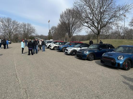 Mini coopers in a row in a parking lot with people milling around.