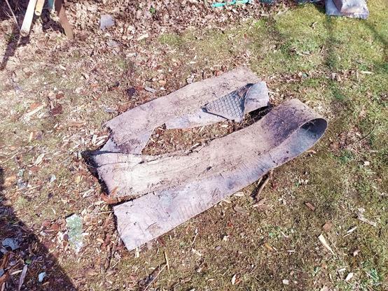 A length of narrow conveyor belt, probably cut to width, folded up and freshly dug out, laying in the grass near where it was found. A corner of rubber floor mat from a vehicle also came up with it.