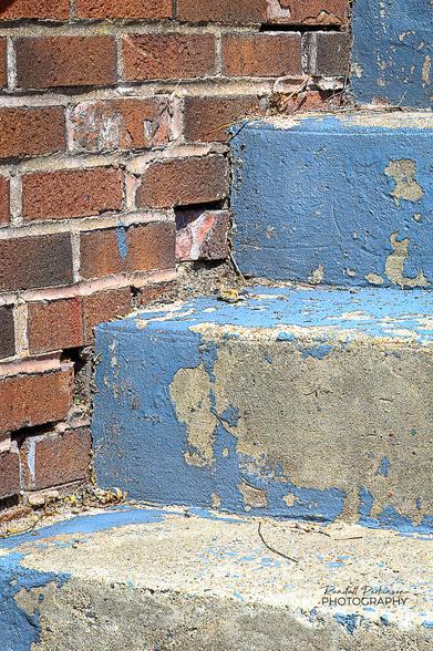 Concrete steps with weathered blue paint next to a decaying brick wall.