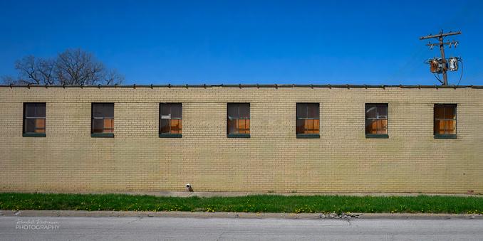 A one story brick building with7 equally sized and spaced windows high on the wall.