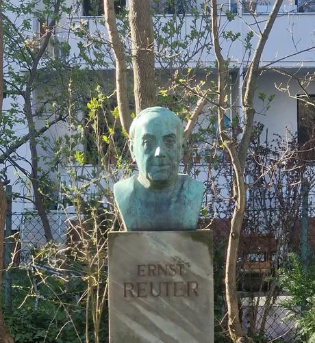 Büste von Ernst Reuter auf einem Sockel mit seinem Namen, umgeben von Bäumen und Sträuchern in einer Wohnanlage an der GartenStraße in Berlin-Wedding.