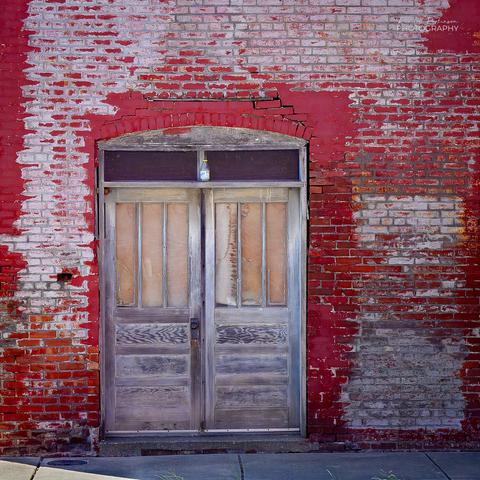 A weathered, unpainted double door in a brick building with red fading paint.