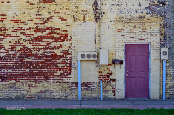 A purple entrance door in a brick wall with faded and peeling yellow paint.