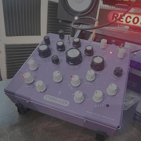 A light purple, rectangular metal enclosure covered with black and white knobs and blinking red LEDs. There’s a constellation motif screenprinted on the console connecting the various knobs. It looks really cool!