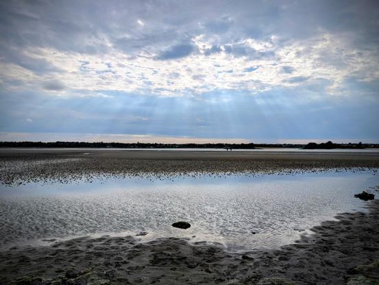 Le reflet du ciel orageux sur la baie à marée basse avec des rais de soleil qui transparaissent.