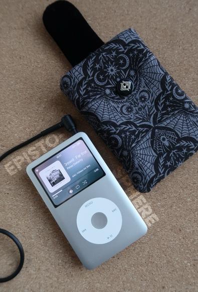 Un iPod avec un écran affichant une chanson de Pete Doherty se trouve à côté d'un étui en tissu noir avec un motif chauve-souris.