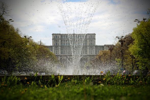 Wasserfontäne aus einer tiefen Perspektive.
Im Hintergrund das Parlamentsgebäude. Alleebäume, die dorthin führen.