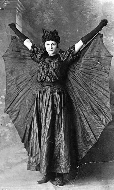 A fierce young woman spreads the wings of her bat costume.