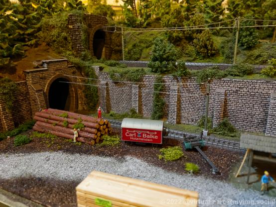A photo of a tunnel entrance on a model railway with wood workers and some logs.