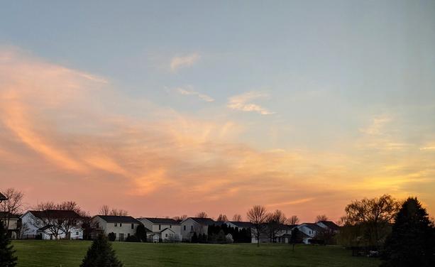 A sunset with reddish clouds over a green field with houses and trees