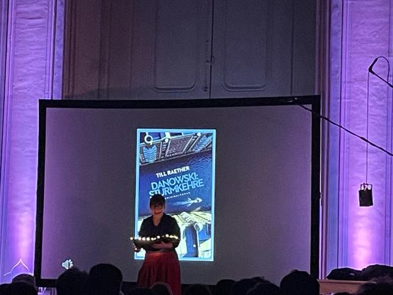 Constanze auf der Bühne vor der Projektion des Covers von Danowski: Sturmkehre