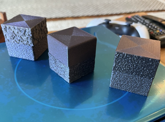 A series of blue/purple 3d printed cubes. Each cube half has a different surface roughness
