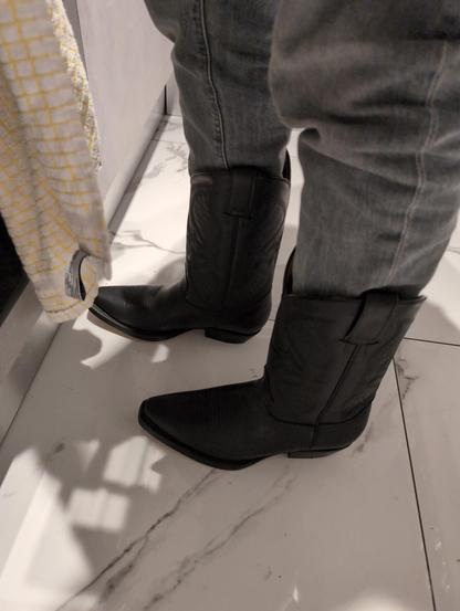 Legs wearing grey jeans and a pair of high cowboy boots. There's a hanging white and yellow cloth hanging on the side, indicating the picture has been taken on a kitchen