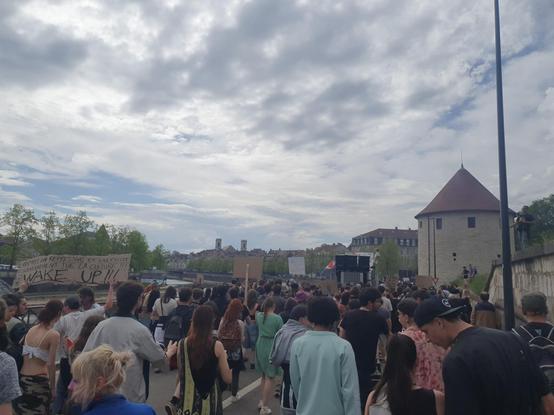 Sur les quais de Besançon, des gens de dos manifestoient  ; avec des pancartes face à un char et un petit soundsystem