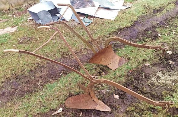 Two plows with handles for steering and an adjustable hitch for pulling by a draft animal. One is a double type with adjustable width, the other a more odern plough with replaceable share.