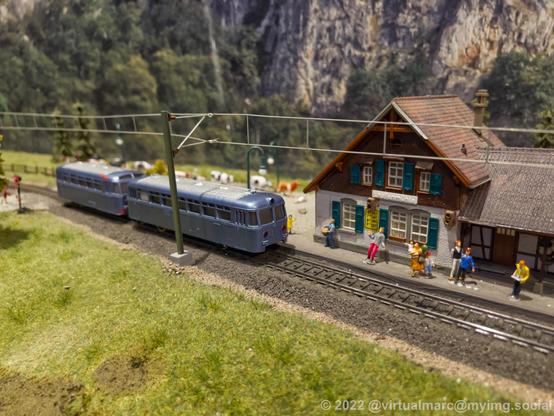 A photo of a model railway with a rail bus in front of a small train station.
