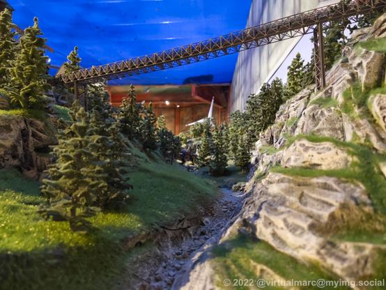 A photo of a canyon between two mountains with trees. A railway bridge is going over the canyon from mountain to mountain.