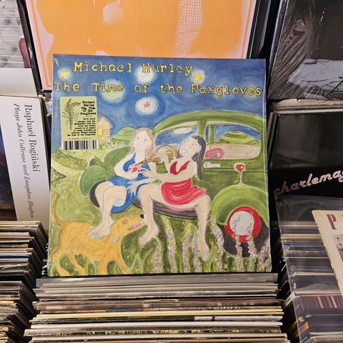 Album cover features a Snock illustration of two women sitting on the running board of a green car, one in a red dress pouring a glass of red wine,  and the other in a blue dress resting her feet on a happy looking dog.