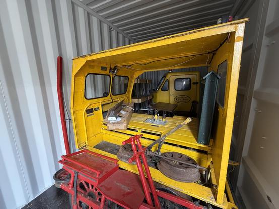 A red track velocipede (track bike) in the foreground, then a yellow open-frame vehicle behind that, and a yellow closed-cab vehicle in the far background