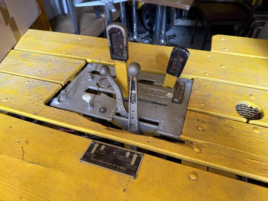 A silver control panel inset in a yellow wood floor, with four levers and three buttons on it