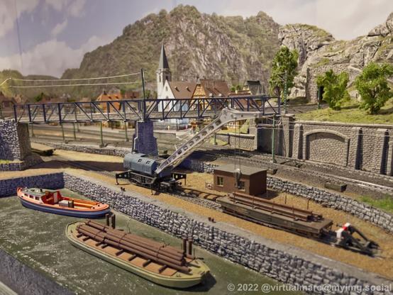 A photo of a log port of a model railway with a boat full of logs and a port crane.