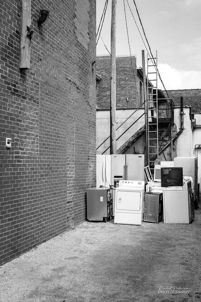 Various different appliances sit in an alley behind a small town shopping district appliance store.