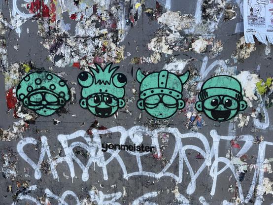 The heads of four character spray painted on a wall in green paint with black outline. The characters sort of look like Super Mario characters, but I don’t think they are. There is a name under the heads that says “Yonmeister”. The art appears to be made with use of a stencil.
