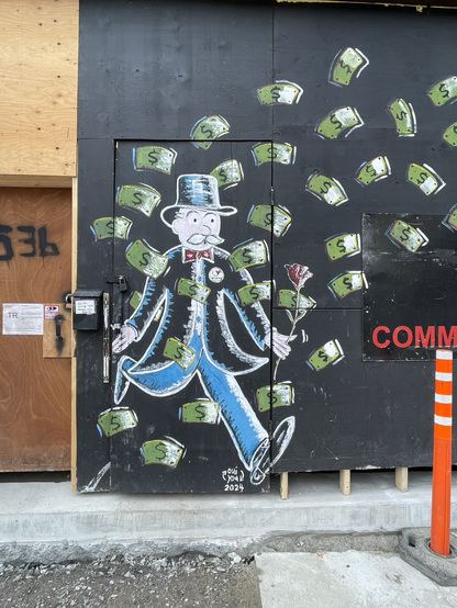 A street murale depicting the capitalist character from the Monopoly board game holding a rose and surrounded with dollar bills. He wears a pin on his coat saying « I[heart]Villeray, the Montreal neighborhood where this murale cn be found.
