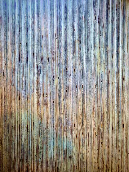 Numerous slats of wood are pressed together in a vertical arrangement, varying from the colors brown to blue to green throughout.