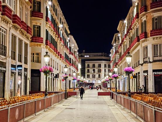 A deserted city street. It is night, but the street is brightly lit. The street is lined with 19th century buildings and temporary seating.