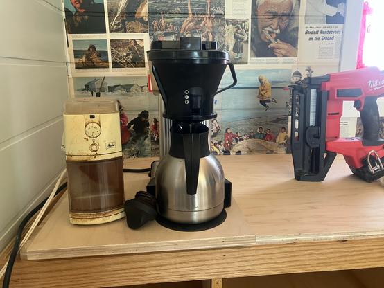 A coffee mill and a Technivorm coffee maker sit on a temporary counter next to a Milwaukee cordless brad nailer.
