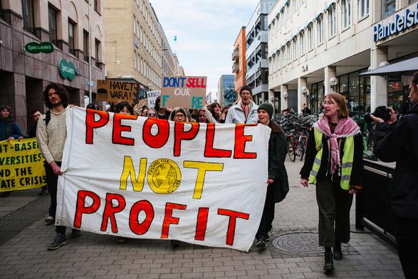 In the front of the protest folks walking with big banner which says "PEOPLE NOT PROFIT".