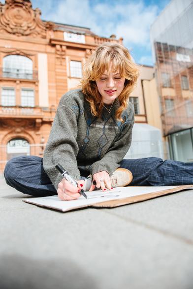 A girl sitting on the ground and drawing a placard.