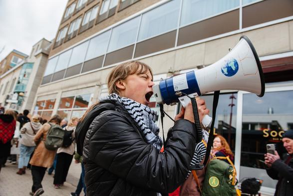 Greta raising slogan in the protest and folks taking photos of her on mobile while walking along in the protest.