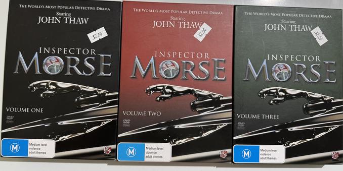 Three DVD covers, each in the same format with a different background colour per season. The boxes are all in the shape / size of VHS tape boxes. Text from top to bottom:

The World's Most Popular Detective Drama.
Starting John Thaw.
Inspector Morse.
Volume …

The letter O in Morse contains a picture of the grill and hood ornament of a vintage Jaguar car. The main image on the background of the box is the hood ornament of that car, a sleek silver big cat leaping from the front of the car.