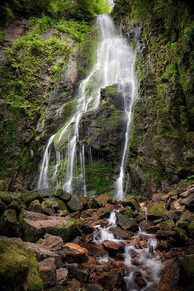 Das Bild zeigt einen Wasserfall mit bemoosten Steinen