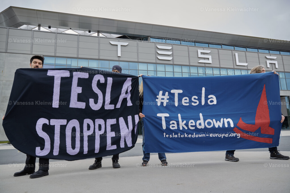 Menschen mit Transparenten "Tesla stoppen" und "#TeslaTakedown. TeslaTakedown-Europe.org" vor der Tesla-Fabrik in Grünheide, Brandenburg.