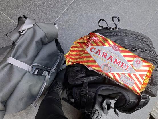 Ein Rucksack auf dem Bahnhofsfußboden stehend, darauf eine Packung mit acht Karamellwaffelriegeln aus schottischer Produktion.