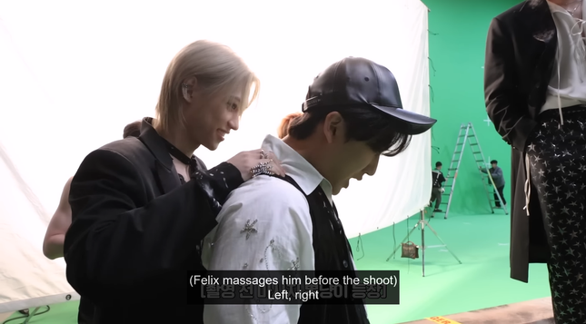 Felix massaging Changbin's shoulders. Changbin's head is bent down and his mouth is open. Felix is happy. Caption: {Felix massages him before the shoot) Left, right